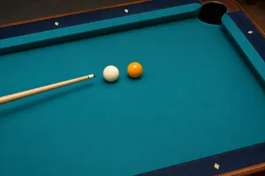 One resting cue ball and one yellow object ball, separated on pool cloth, with the wooden cue tip behind the cue ball and no trajectory traces